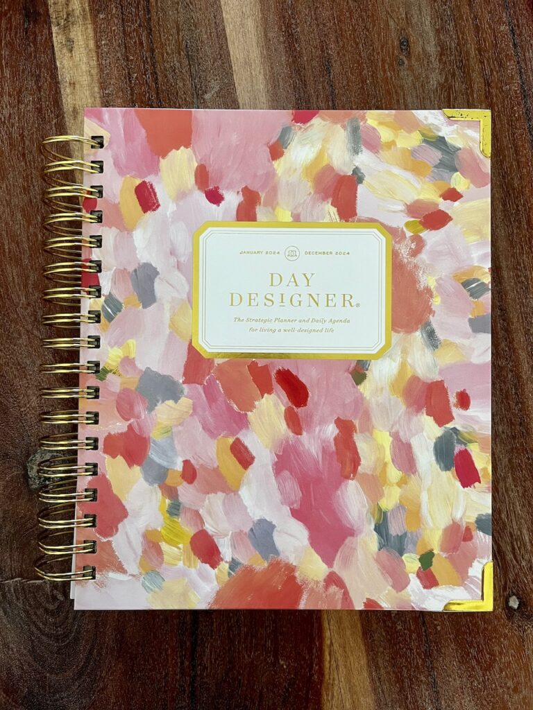 Day Designer Day Planner in a pink and yellow watercolor design lays on a wooden table