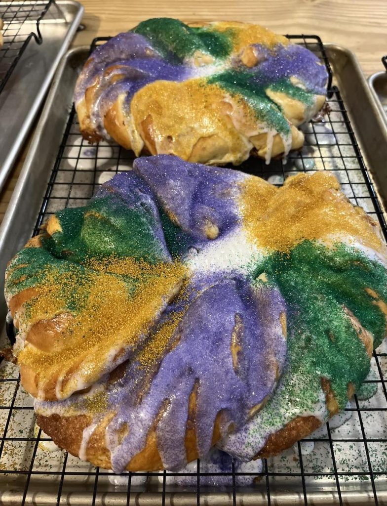 Mardi Gras King cake with purple, green, and gold sprinkles sitting on a cooling rack | King Cake by Beth's Bakery Buns Pensacola