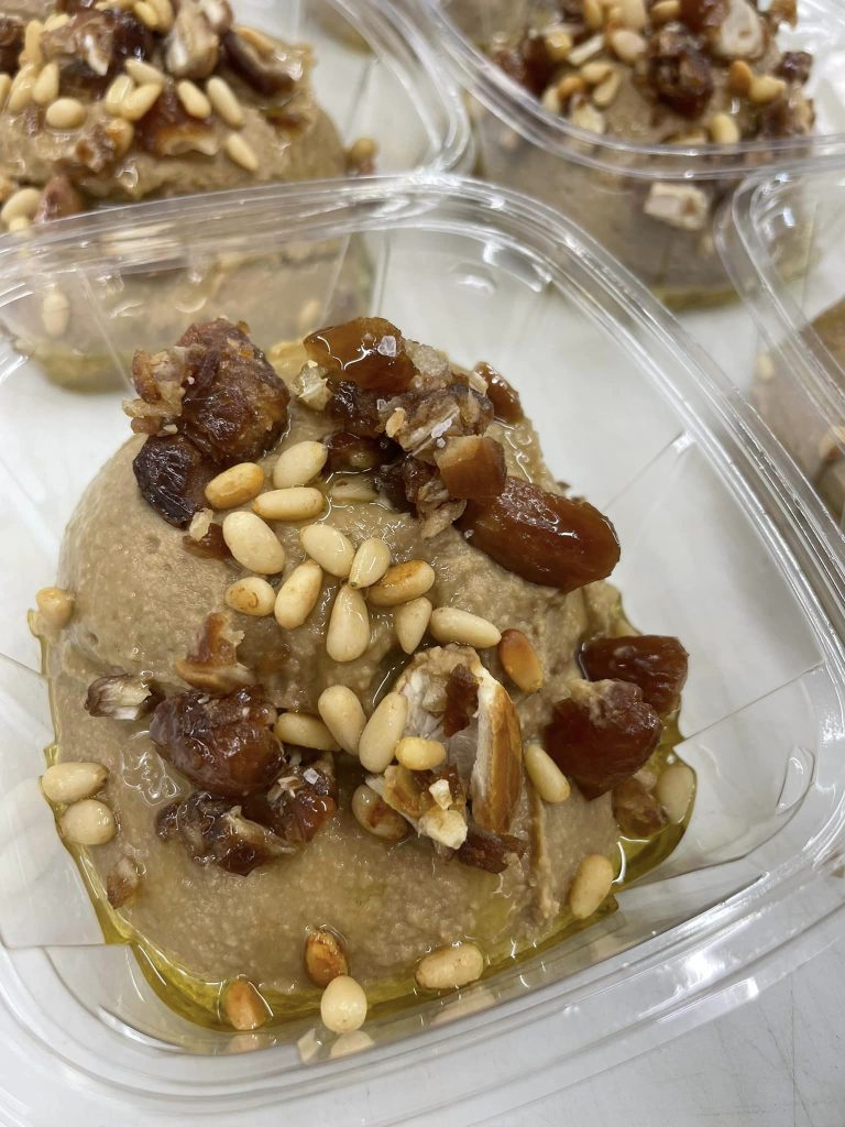 Container of black garlic hummus topped with roasted black garlic and pine nuts | Made by the Hummus Lady Pensacola