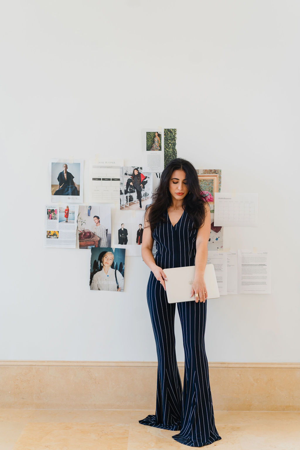 Brunette woman in pinstriped navy blue matching set stands in front of vogue magazine pages taped to a wall