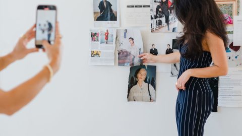 Woman stands in front of a wall covered with Vogue magazine pages while someone takes a picture on mobile phone