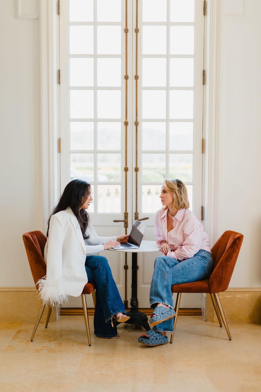 Two women sit at a cafe table and have an engaging conversation in front of a set of french doors | how to have more productive conversations