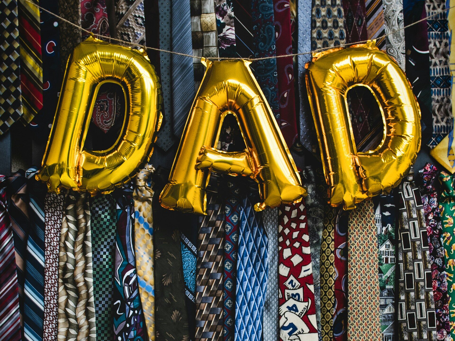 Gold balloons spelling the word 'Dad' against a backdrop of neckties