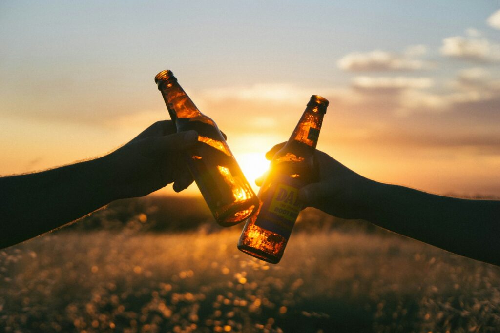 Two people cheers with glass beer bottles for Father's day in front of a sunset backdrop