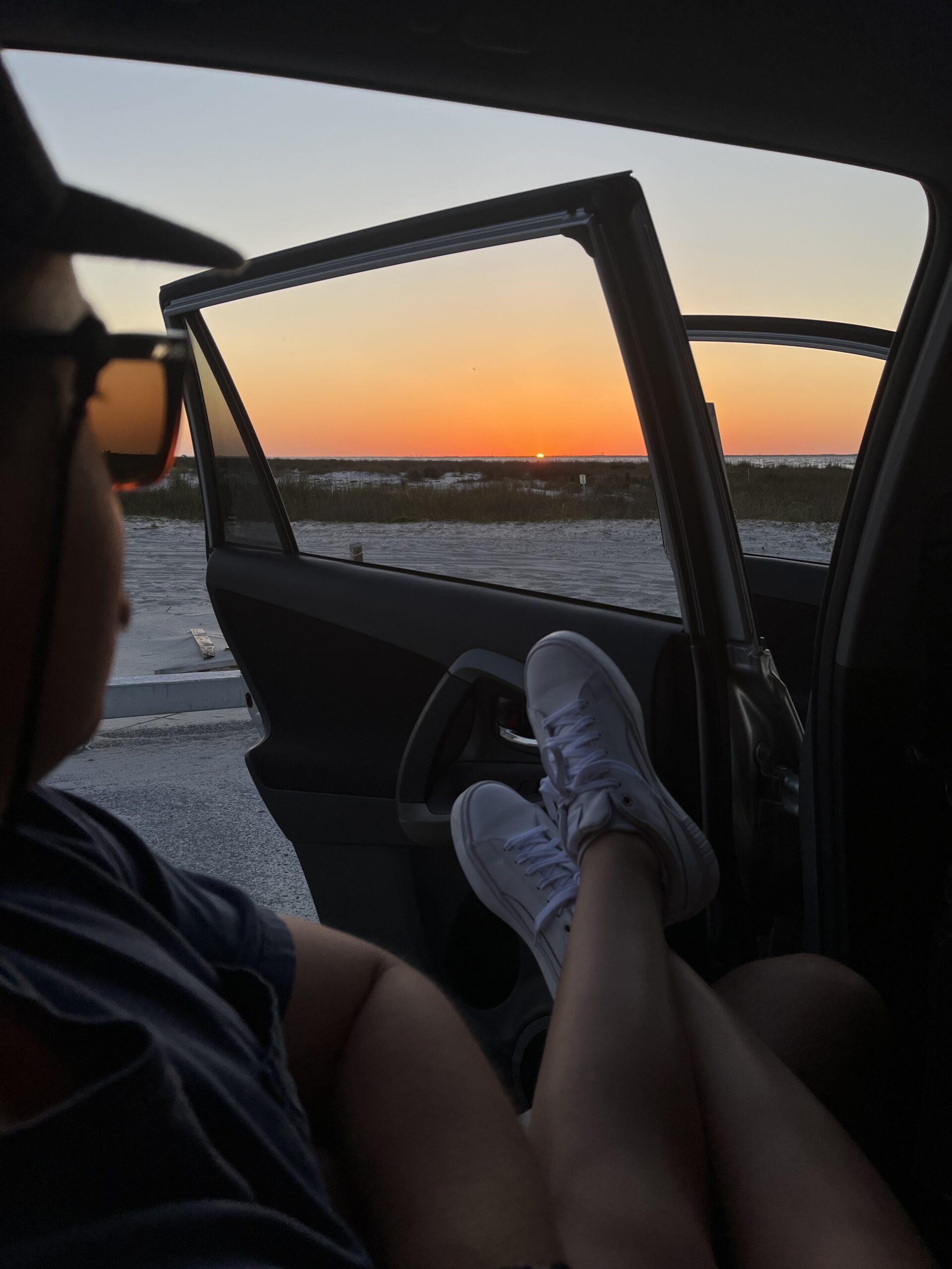 Two people watch the sunset over Fort Pickens on Pensacola Beach out of the backseat of a car