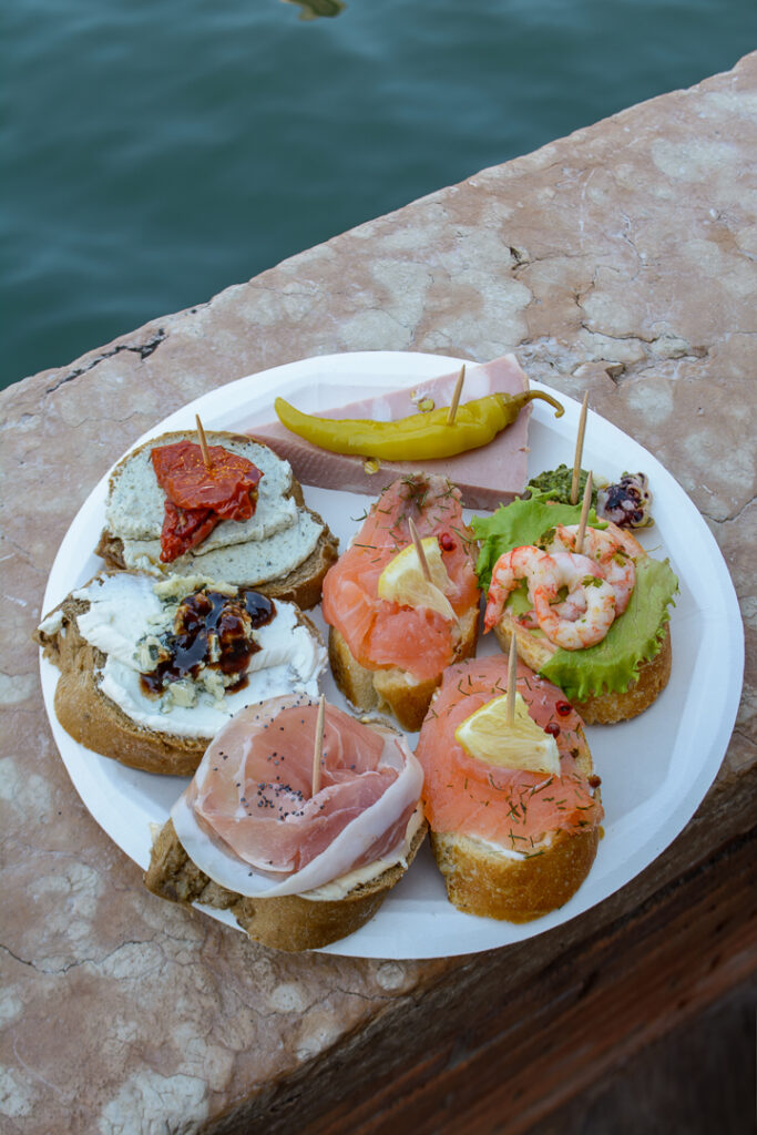 Plate of seven pieces of cicchetti in Venice Italy sits beside the canal
