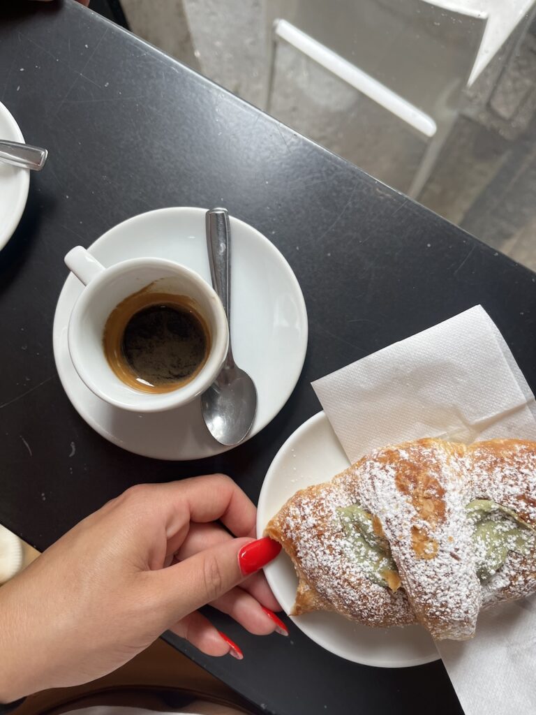 Cup of espresso sits next to a pistachio croissant on a bar in a Milan cafe