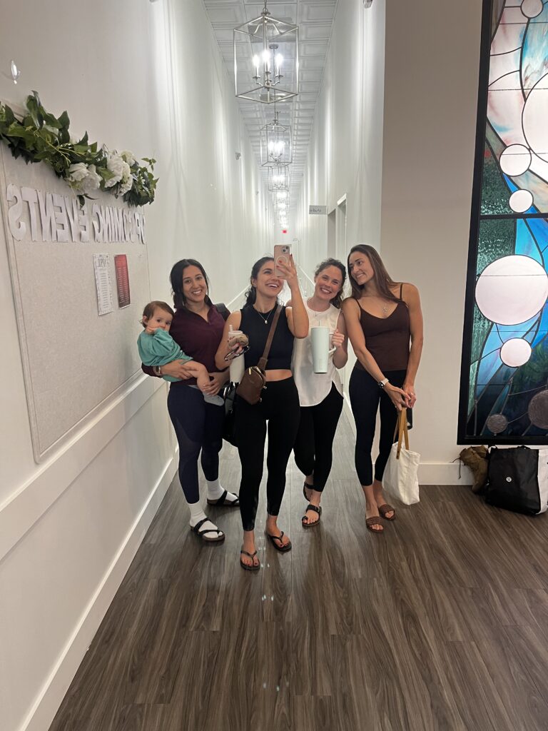 Group of four women take a mirror photo in front of a long hallway at Pure Barre studio
