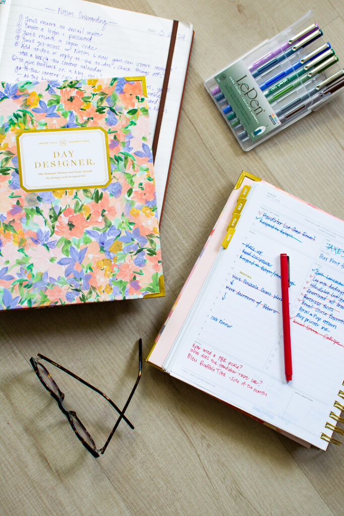 Floral print Day Designer planner and notebook sit next to open page of daily planner next to multi colored pens and a pair of glasses | Lifestyled By Sofia
