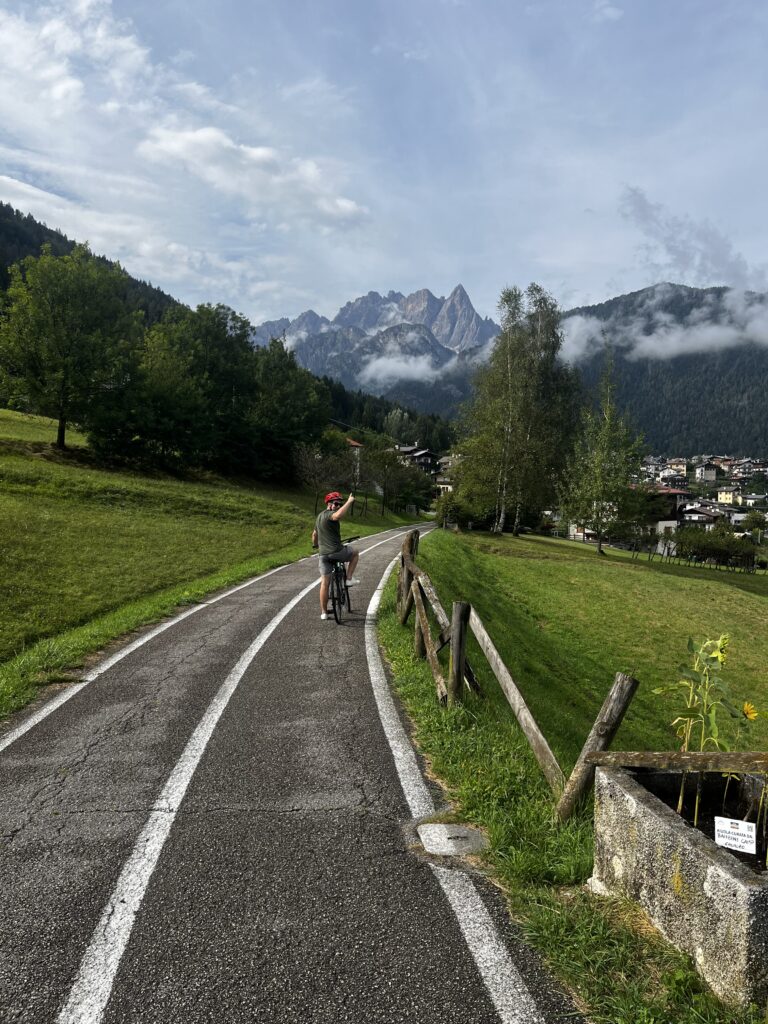 Man waves from his bike while riding a bike path into the Dolomites