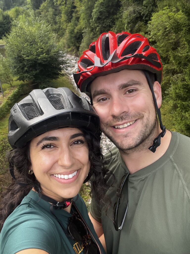 Couple in bike helmets takes a selfie in front of a river through the Dolomites mountain region in northern Italy