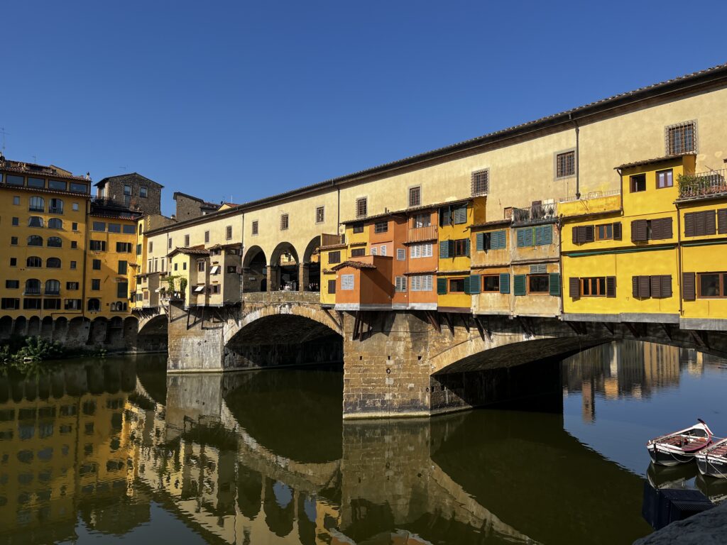 view of the Ponte Vecchio bridge in Florence from the banks of the Arno river | traveling northern Italy by train