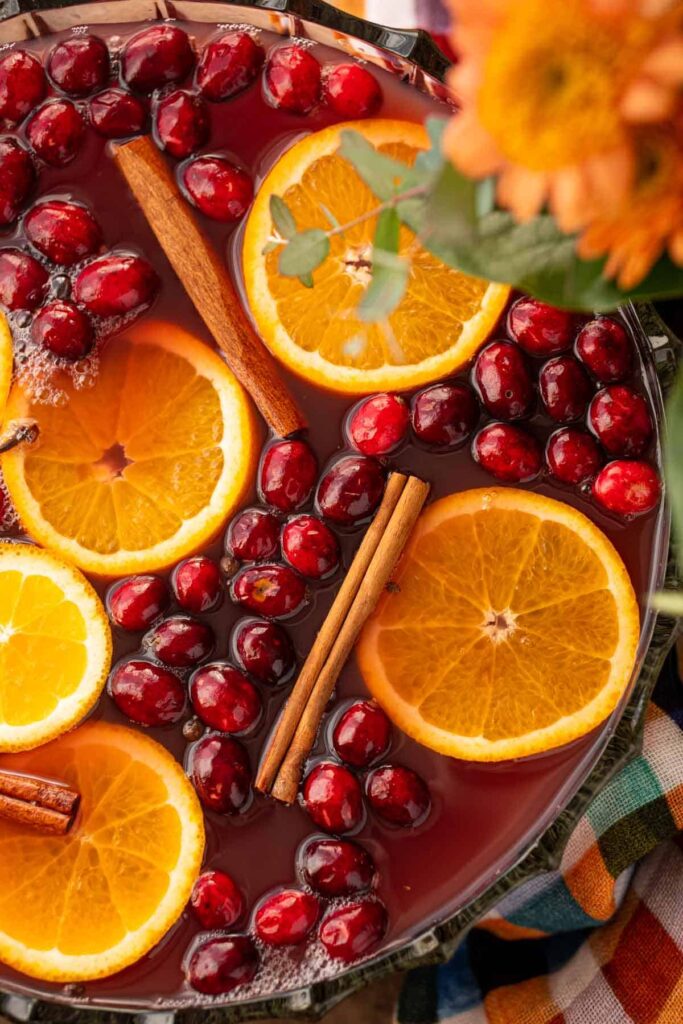 Orange slices, cinnamon sticks, and cranberries float in an Autumn Punch in a glass punch bowl | Festive Thanksgiving Mocktails roundup by Lifestyled By Sofia 