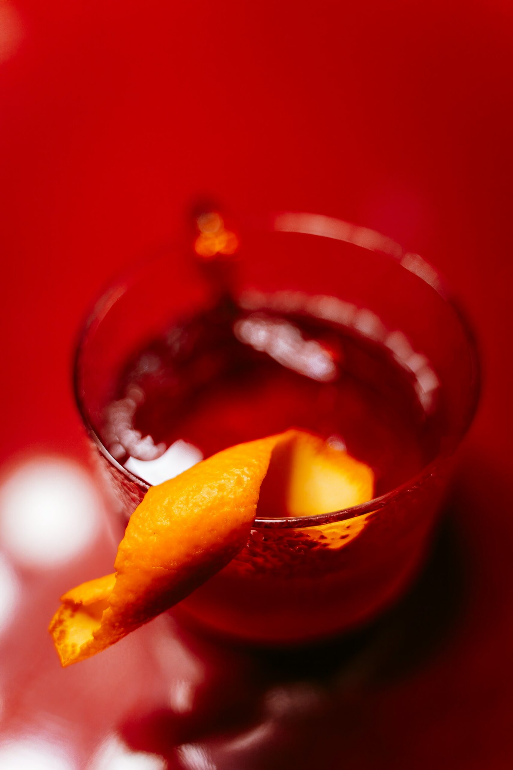 Festive Thanksgiving Mocktail in a short glass with an orange rind on the rim sits on a red tabel | Lifestyled By Sofia Mocktail Roundup