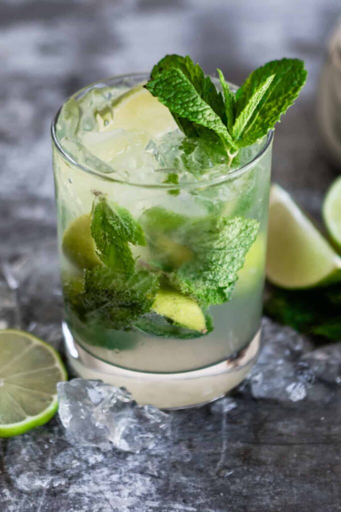 Virgin Mojito Mocktail sits on a concrete countertop surrounded by cut limes | Seasonal Mocktails Roundup by Lifestyled By Sofia