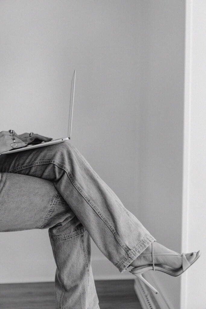 Crossed legs in jeans and stiletto heels prop up a Macbook Air laptop as someone types on the keyboard | email marketing best practices for small business owners blog by Sofia Brown