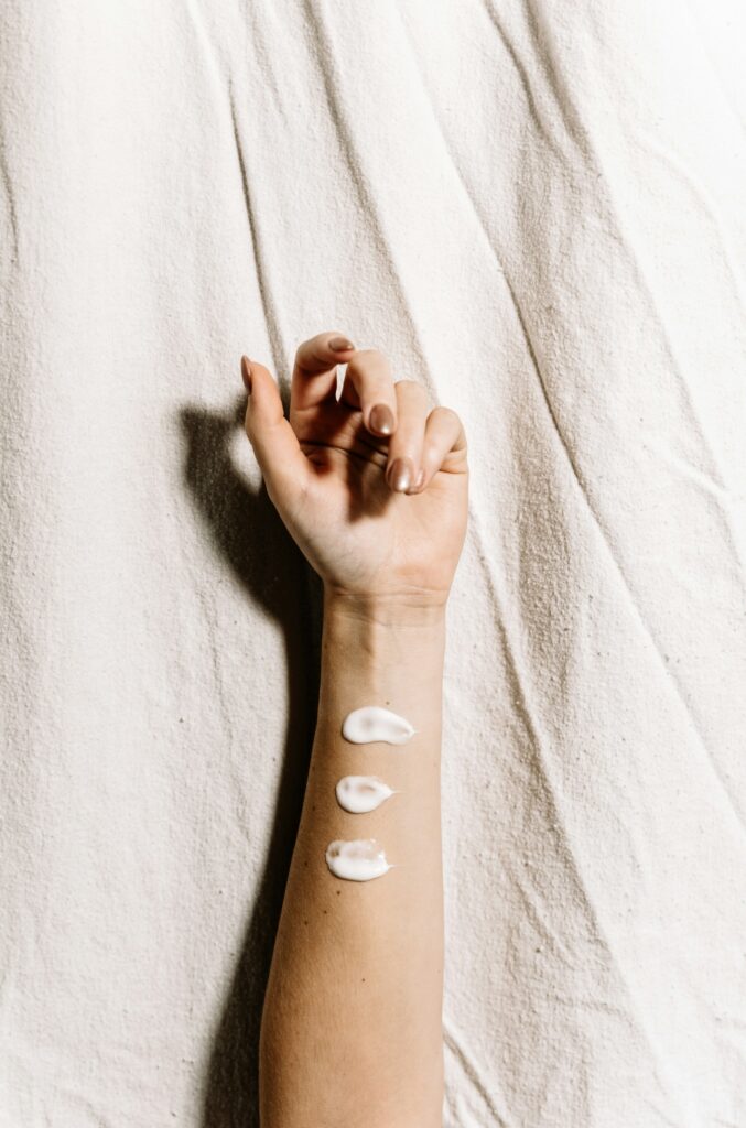A forearm with three streaks of lotion rests on a white blanket featuring some of the best affordable face creams